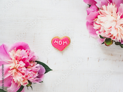Fototapeta Naklejka Na Ścianę i Meble -  Bright flowers and pink, glazed cookie with the word MOM on a white, isolated background. Top view, close-up. Happy family concept