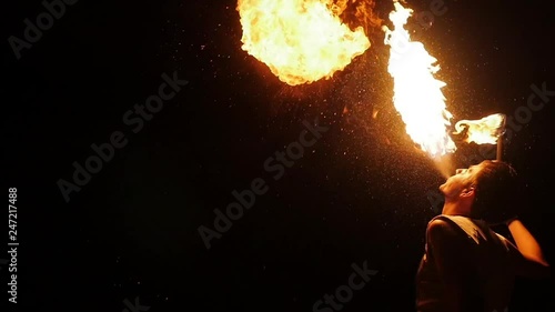 Enjoyment concept entertaining tourists. Professional actor showing flamy spectacle. Young man standing and diffuse in air flaming splash from mouth. Riskily workmanship presentation at darkness area photo
