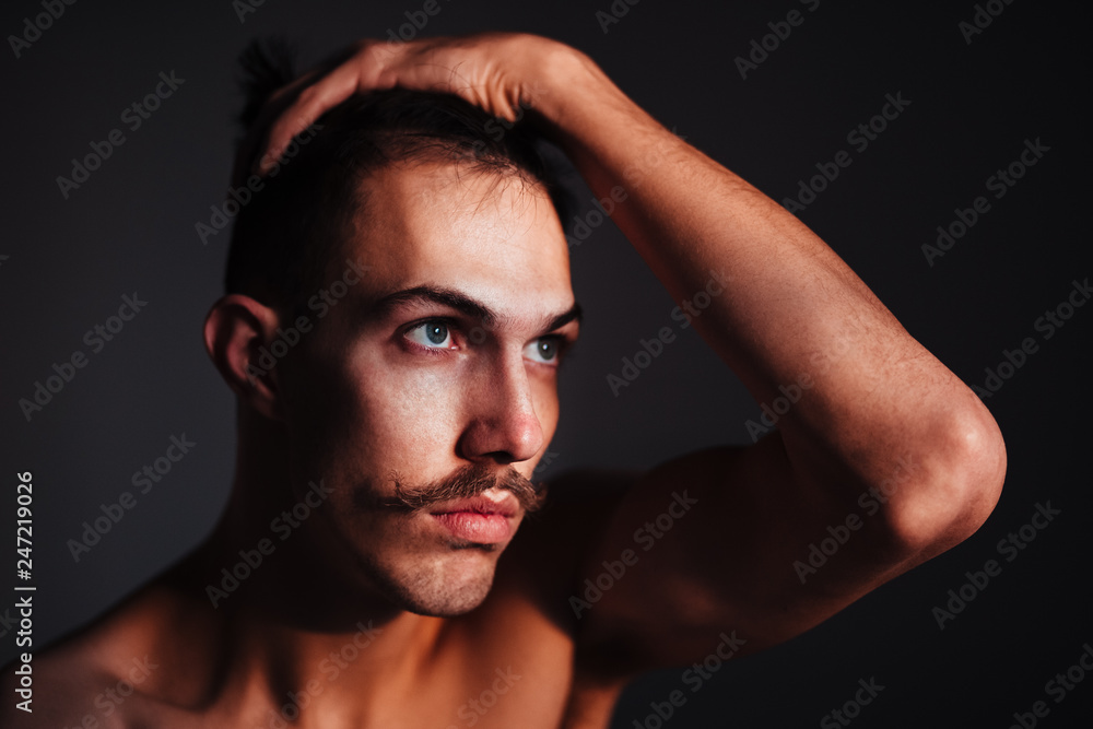Young shirtless man with mustache thinking by the window