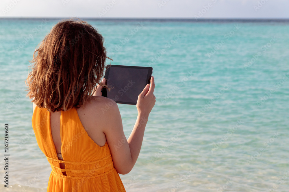 young woman standing in front of the sea and using her tablet during sunset young woman standing in front of the sea and using her tablet during sunset