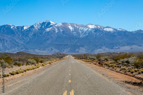 Looking along a long straight road in New Mexico, with snow capped mountains in the distance