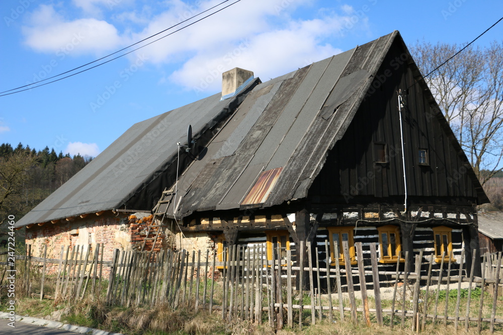 An old, ruined house built of wood and brick. Roof covered with shed felt. Wooden fence. Pleasant, warm, sunny, calm day in the countryside. Spring in the mountains.
