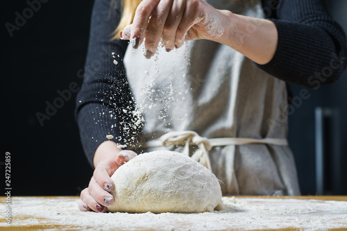 The chef sprinkles flour on the yeast dough on a wooden table. Side view, wooden background