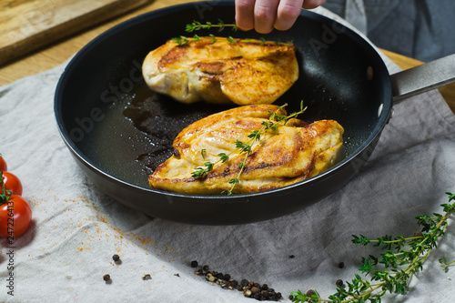 Chef sprinkles thyme on chicken Breasts in a frying pan. Background kitchen, side view