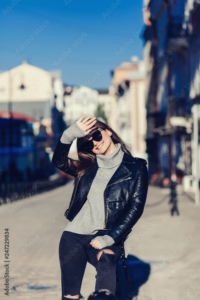 happy woman in sunglasses and leather jacket posing in the city