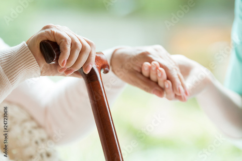 Photography Closeup of elderly lady holding walking cane in one hand and holding volunteer's