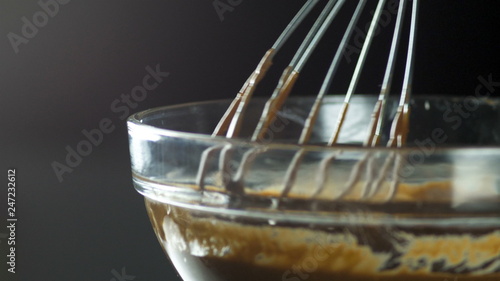 Liquid chocolate in a glass container. The corolla rises above the glass container and the shekolad flows in a small stream. Confectionery. A confectioner prepares a dessert, sauce. photo