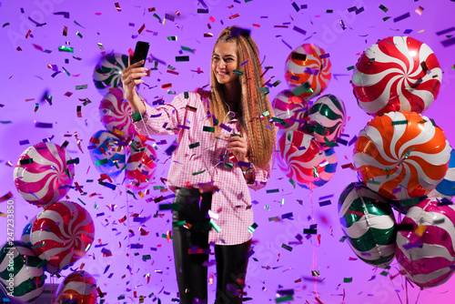  Girl in headphones with a smartphone, sings a song, on a purple background of candy, colored balloons