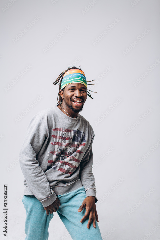 Fototapeta premium Portrait of a smiling black young model in a gray sweater and blue pants on a gray background