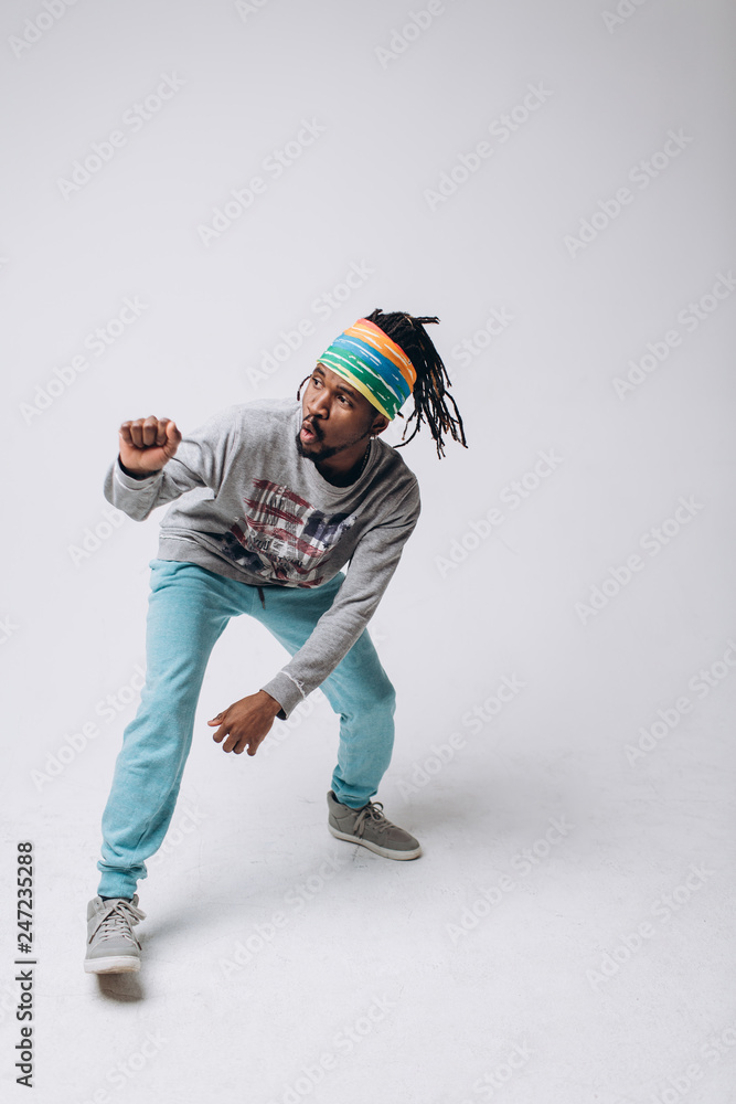 Fototapeta Portrait of a smiling black young model in a gray sweater and blue pants on a gray background