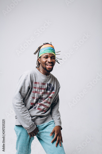 Portrait of a smiling black young model in a gray sweater and blue pants on a gray background