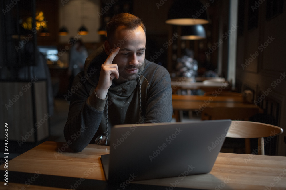 Young confident man working at laptop in cafe. Young confident man working at laptop in cafe.