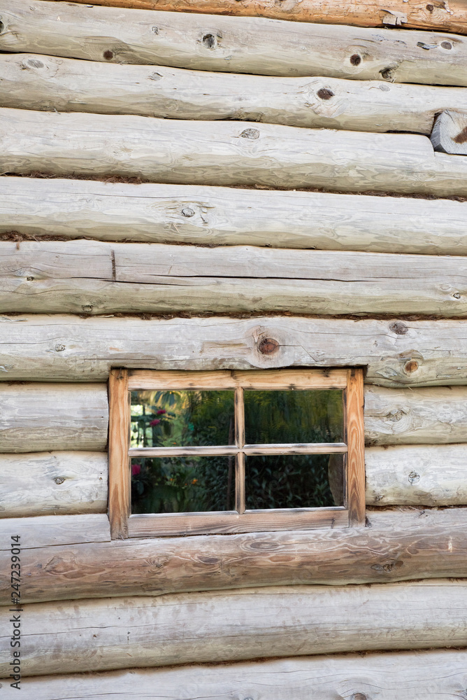 Rustic wooden house made of round logs. Abandoned villages and houses. Ancient window design. Wooden window frame. Age-old buildings. Reflection of summer flowers in the window. Rustic wooden house made of round logs. Abandoned villages and houses. Ancient window design. Wooden window frame. Age-old buildings. Reflection of summer flowers in the window.