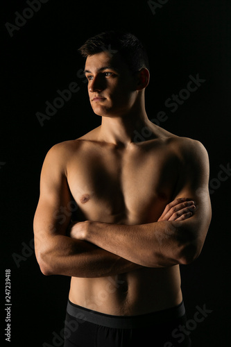 Portrait of a man with a beautiful athletic body in a low key. Pumped up guy with a naked torso.
