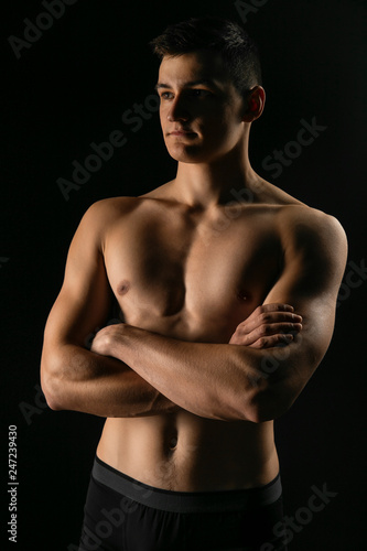 Portrait of a man with a beautiful athletic body in a low key. Pumped up guy with a naked torso.