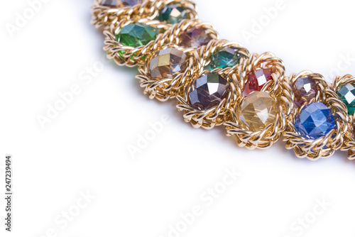 Necklace of gold chains, adorned with colorful beads. Female necklace on a white background. A round gold metal necklace with blue, red, yellow, green, purple crystals. Closeup. Place for text.