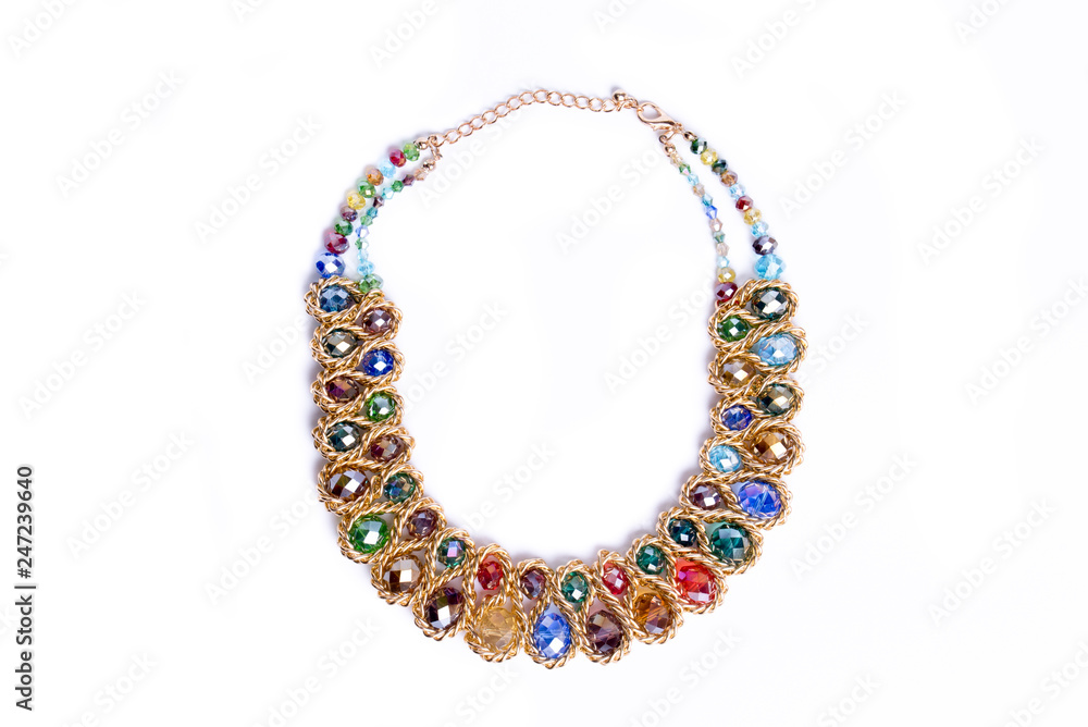 Costume jewelry, factory-produced mass product. Golden look necklace with colored glass gemstones isolated on white background. Top view.Beautiful jewelry with green, red, blue, brown, yellow, purple Costume jewelry, factory-produced mass product. Golden look necklace with colored glass gemstones isolated on white background. Top view.Beautiful jewelry with green, red, blue, brown, yellow, purple