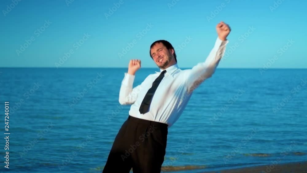 Excited businessman screaming and raising hands to the sky by the sea, slow motion Excited businessman screaming and raising hands to the sky by the sea, slow motion