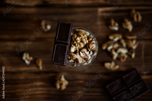 Chocolate slices and peeled walnuts lie on a brown wooden surface. Rustic still life. Healthy food
