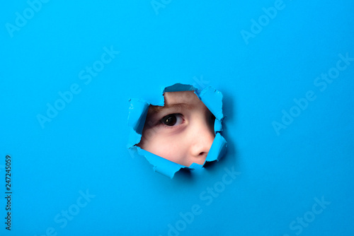 Through paper. Spy eye watching through a hole. Kid looking through paper. Child's eye looking through hole. Boy breaks paper. photo