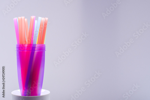 Bright multi-colored plastic tubules in a purple glass on a white background, an empty place to insert text