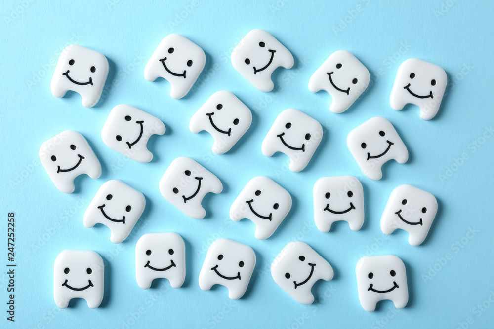 Many small plastic teeth with cute faces on color background, top view Many small plastic teeth with cute faces on color background, top view