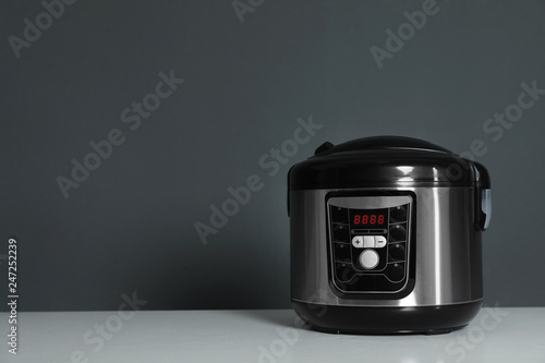 Modern electric multi cooker on table against dark background. Space for text
