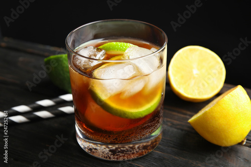 Glass of cocktail with cola, ice and cut lime on table against black background