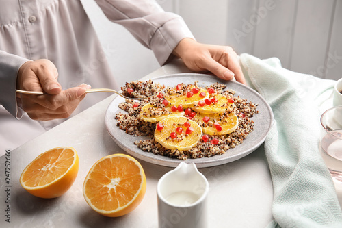 Woman eating quinoa porridge with orange and pomegranate seeds at table, closeup