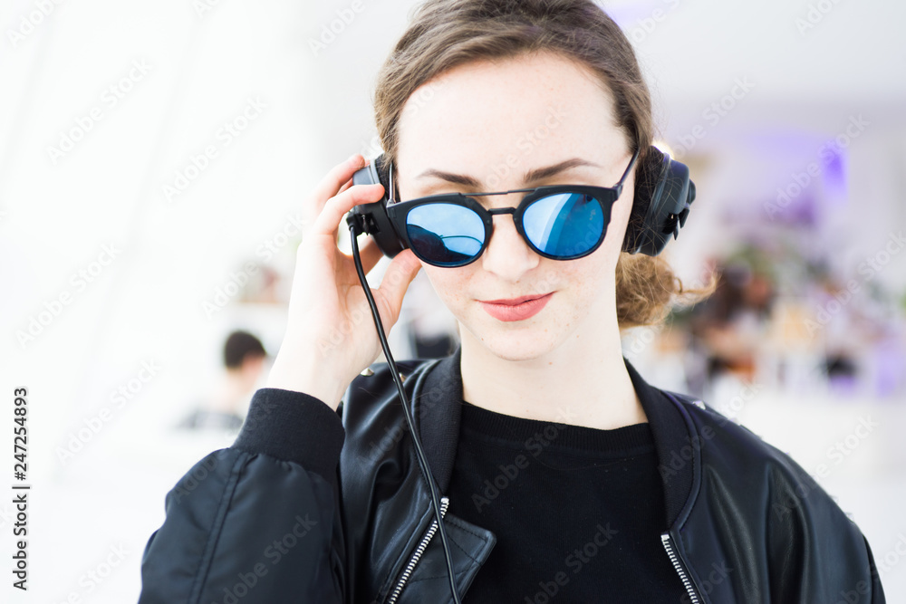 Young red hair girl dj with trendy style wearing leather jacket and super  azure glasses posing in a confident way with headphones Stock Photo | Adobe  Stock