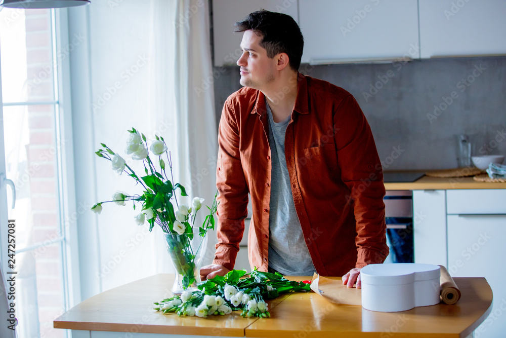 Young man wrapping wite roses on a table at kitchen Young man wrapping wite roses on a table at kitchen