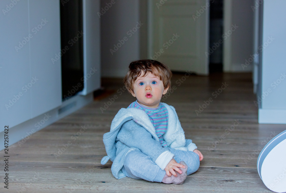 Little baby sitting on a floor at home at kitche