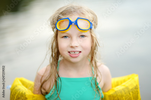 Cute young girl wearing swimsuit playing by a river on hot summer day. Adorable child having fun outdoors during summer vacations.