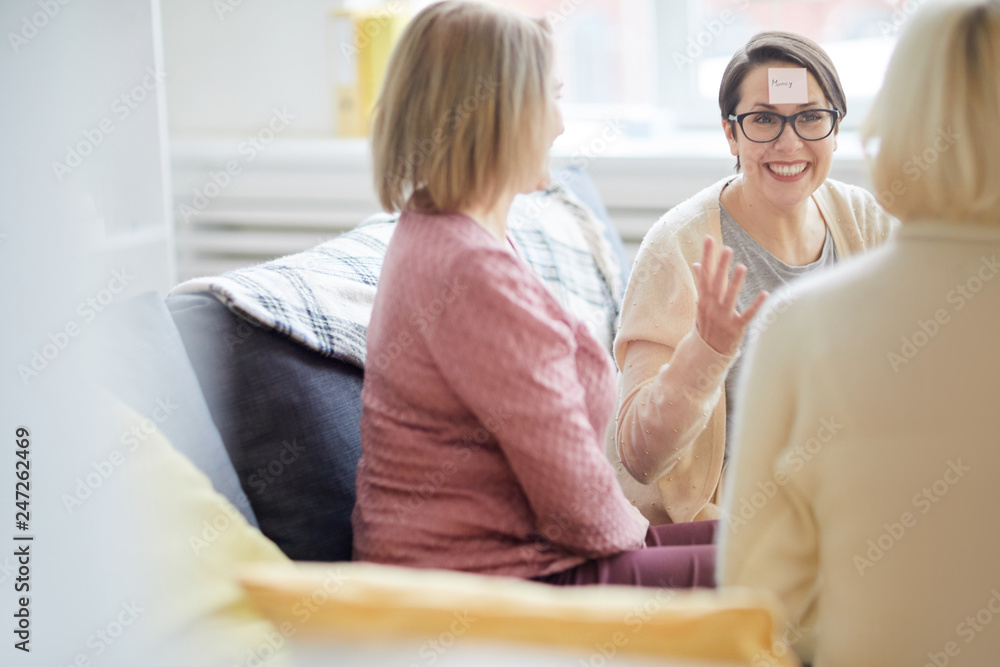 Portrait of three adult women playing games and having fun at home, focus on laughing woman with sticker on head, copy space