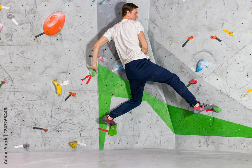 Rock climber man hanging on a bouldering climbing wall, inside on colored hooks Rock climber man hanging on a bouldering climbing wall, inside on colored hooks