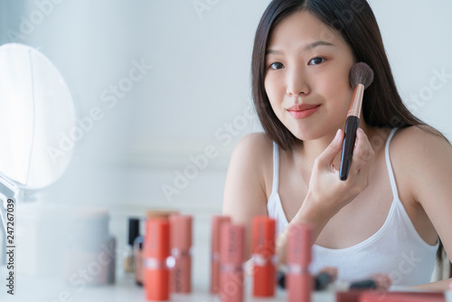 beautiful asian woman white tshirt smile with happiness hand hold blush on and makeup cosmetic items in bedroom with healthy face skincare concept