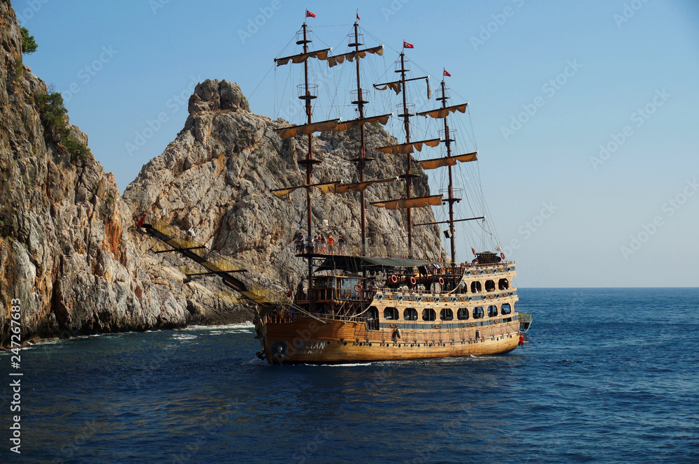 Tourists enjoying sea trip on board of a sailboat in front of impressive cliffs in Mediterranean sea beside the shoreline of Turkish city Alanya. Antalya, Turkey. Tourists enjoying sea trip on board of a sailboat in front of impressive cliffs in Mediterranean sea beside the shoreline of Turkish city Alanya. Antalya, Turkey.
