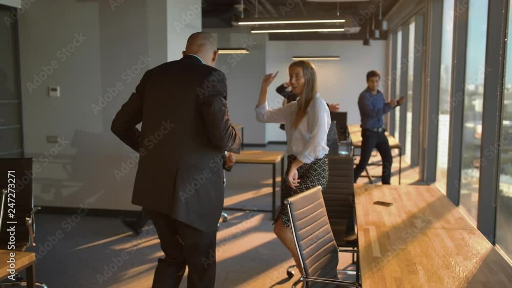 Businesspeople dancing cheerfully in office in front of the camera ...