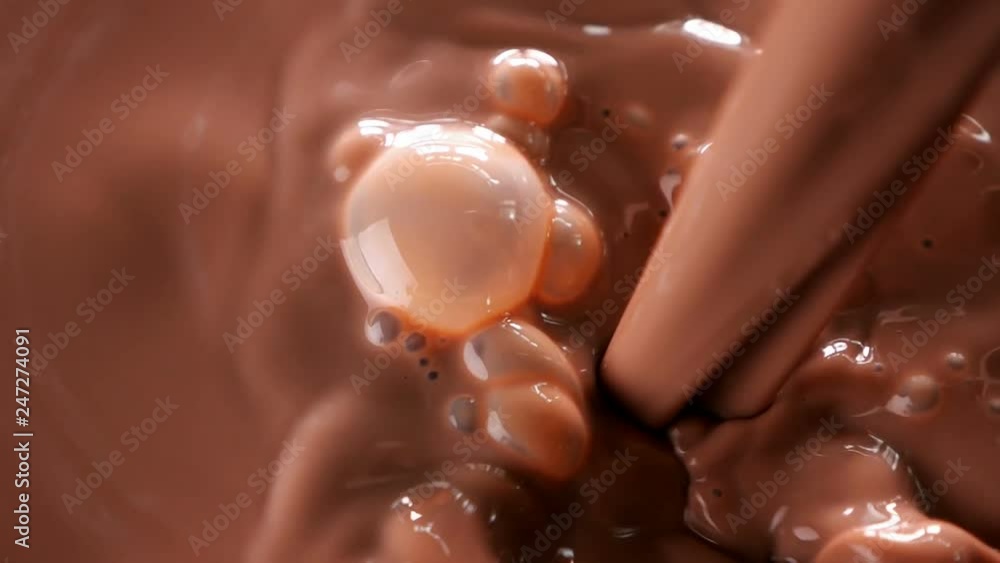 Chocolate milk pouring. Stream of cocoa drink create a swirl and bubbles - top view, slow motion