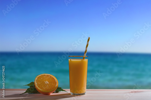 a glass of freshly squeezed orange juice on a beach with azure water on a trip