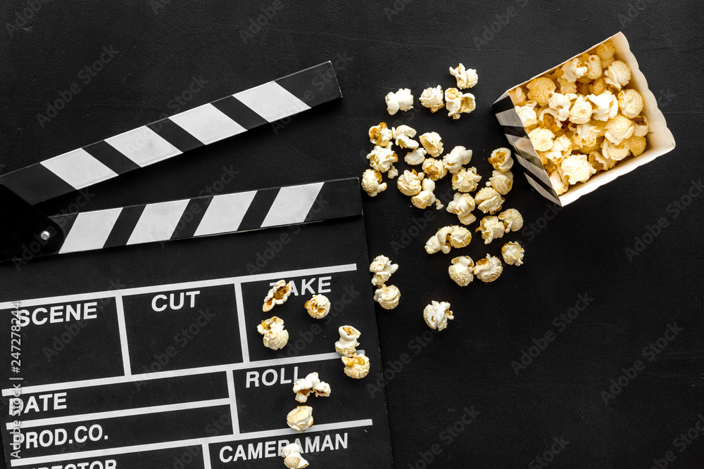 Film watching concept. Clapperboard and popcorn on black background top view copy space