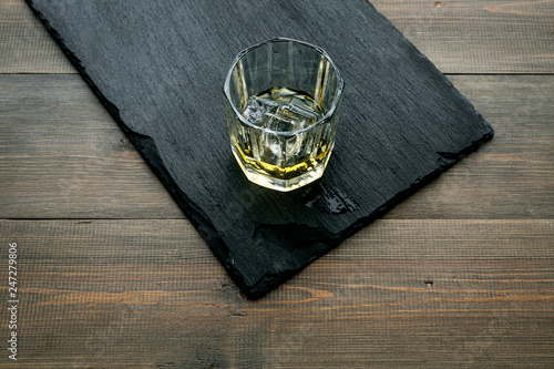 In the bar. Whiskey with ice on black desk on wooden background top view copy space
