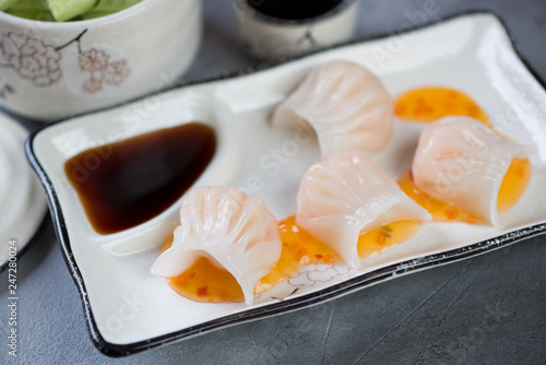 Closeup of steamed prawn hargows with dipping sauces on a white plate, selective focus photo