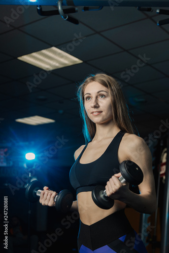 Young and beautiful woman working out with dumbbells in gym. Biceps curls.