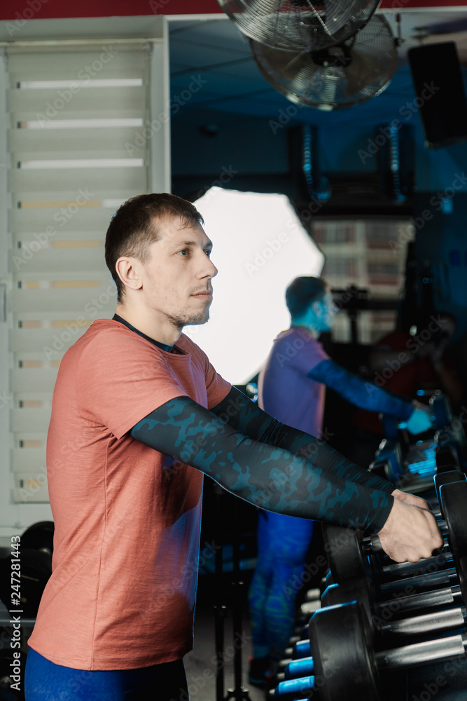Handsome athletic man takes dumbbells from the racks for further training in the gym. Handsome athletic man takes dumbbells from the racks for further training in the gym.