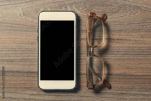 Smartphone and reading glasses on an old wooden board