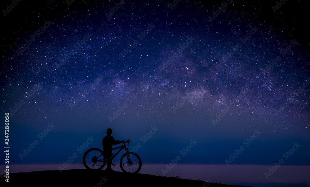 Obraz premium Boy and bike on the mound and the Milky Way in the sky; Long exposure photograph, with grain.Image contain certain grain or noise and soft focus. 