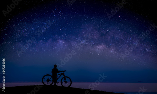 Boy and bike on the mound and the Milky Way in the sky; Long exposure photograph, with grain.Image contain certain grain or noise and soft focus. 