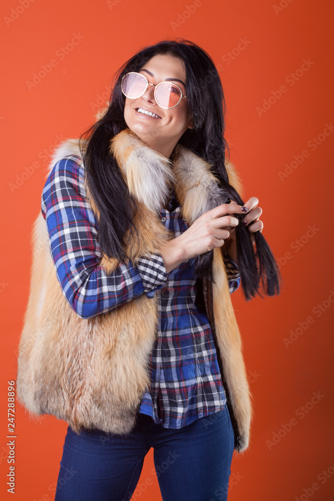 Beautiful sexy lady fashion pretty woman model pose wear plaid shirt and fur vest on the orange studio background Beautiful sexy lady fashion pretty woman model pose wear plaid shirt and fur vest on the orange studio background