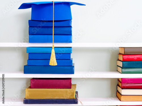 Graduation blue mortarboard on top of stack of books on wooden shelf photo